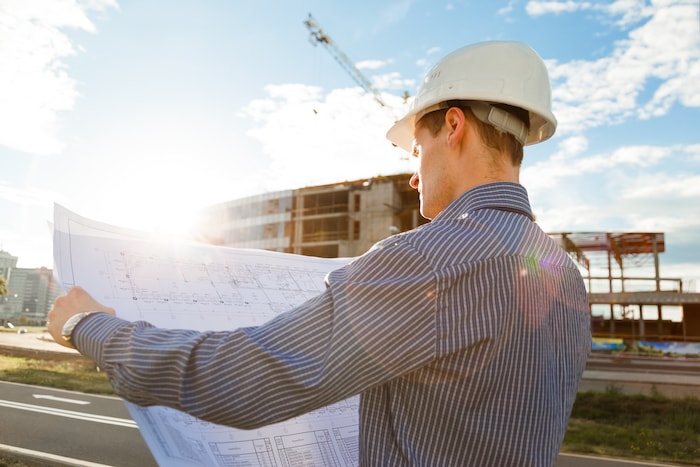 architect-in-helmet-with-blueprints-looks-at-ppqn725-min architect-in-helmet-with-blueprints-looks-at-ppqn725-min